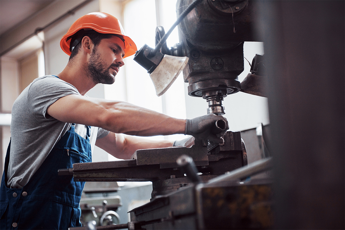 Experienced operator in a hard hat. Metalworking industry concept professional engineer metalworker operating CNC milling machine center in manufacturing workshop.