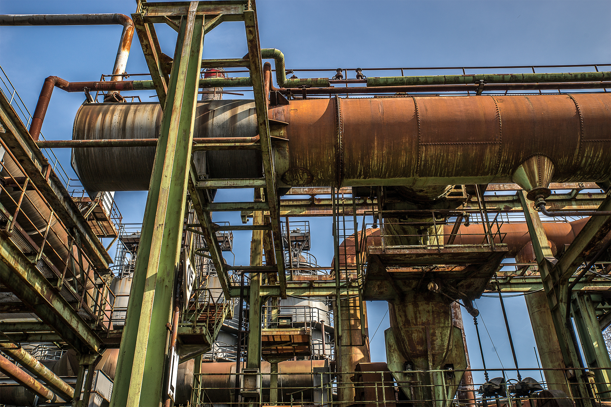 A low angle shot of metal structures and pipes with a clear sky